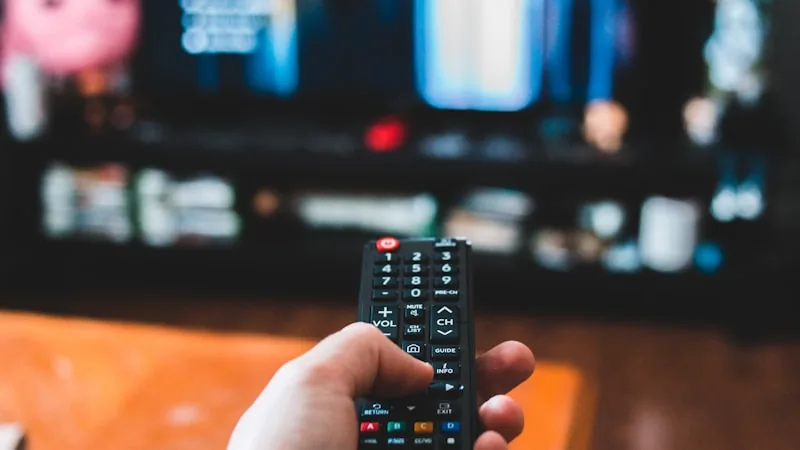 Person holding a traditional cable TV remote pointed at a television