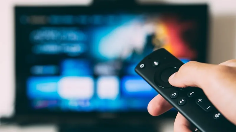 Hand holding a streaming remote pointed at a TV showing an IPTV interface